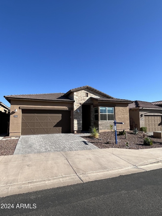 view of front of home with decorative driveway, stone siding, a garage, and stucco siding