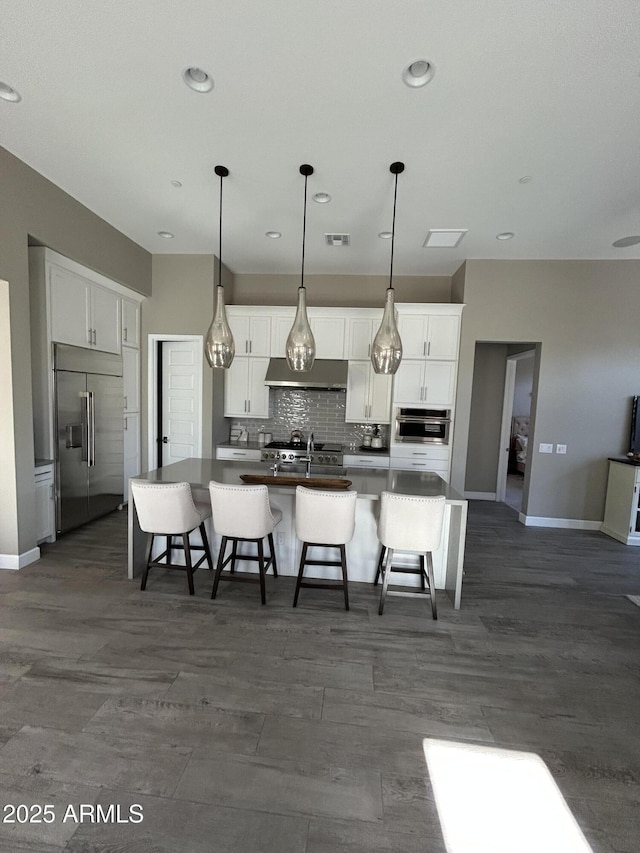 kitchen featuring appliances with stainless steel finishes, white cabinets, a kitchen island with sink, and backsplash