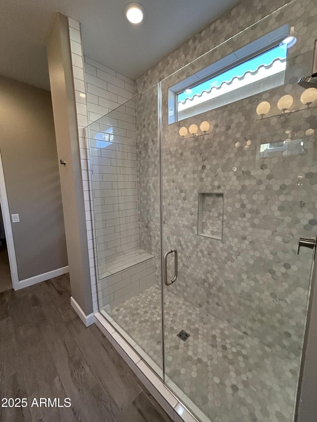 bathroom with a stall shower, wood finished floors, and baseboards