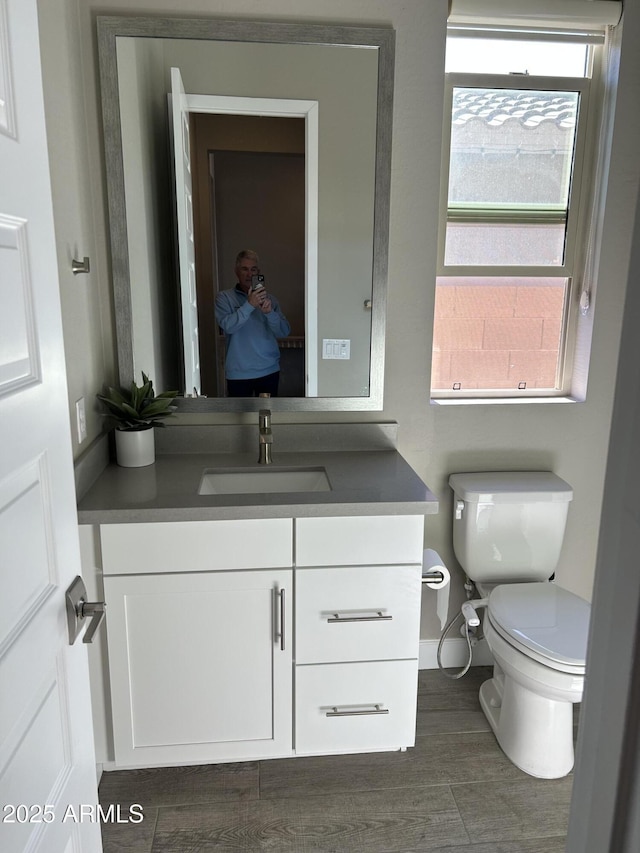 half bathroom with toilet, wood finished floors, and vanity