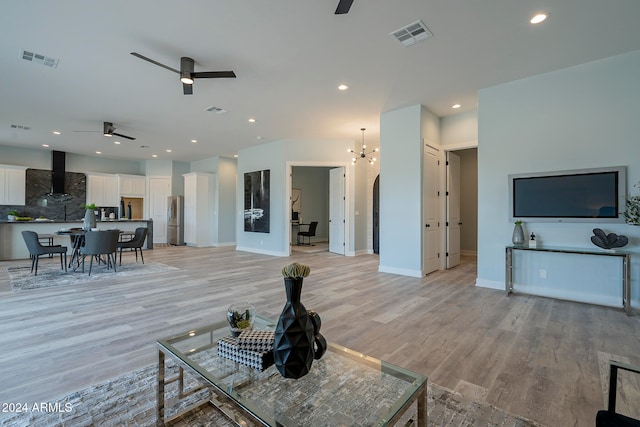 living room featuring ceiling fan with notable chandelier and light hardwood / wood-style flooring