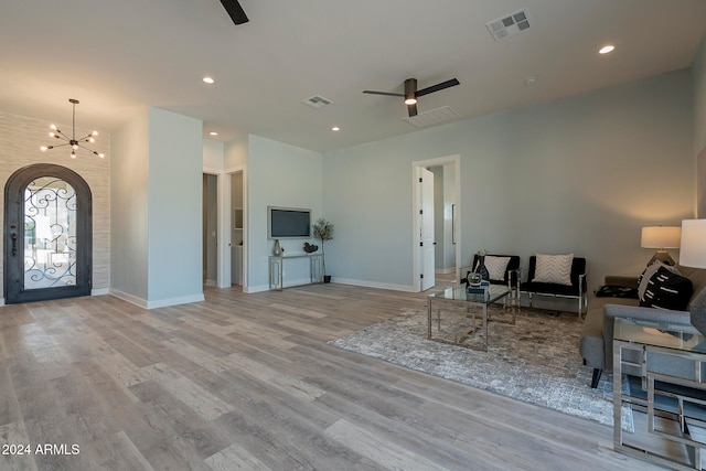 living room featuring ceiling fan with notable chandelier and light hardwood / wood-style flooring