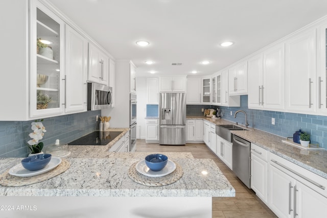 kitchen with stainless steel appliances, sink, white cabinetry, light hardwood / wood-style floors, and tasteful backsplash