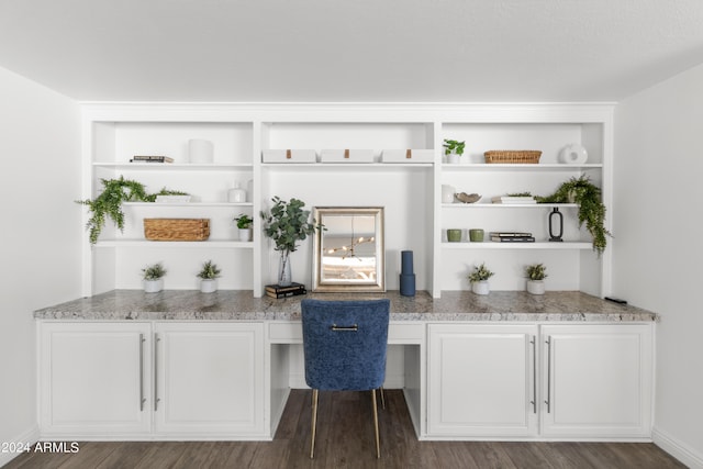 bar with white cabinetry, built in desk, light stone counters, and dark hardwood / wood-style flooring