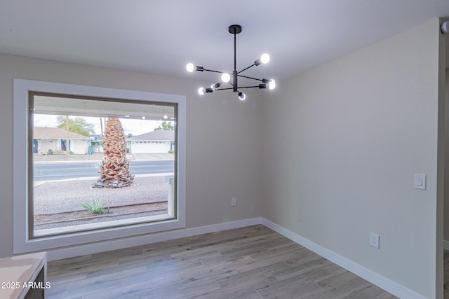 unfurnished dining area featuring a notable chandelier, baseboards, and light wood-style floors