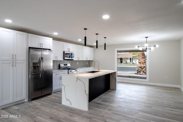 kitchen with light wood finished floors, a sink, stainless steel appliances, white cabinetry, and tasteful backsplash