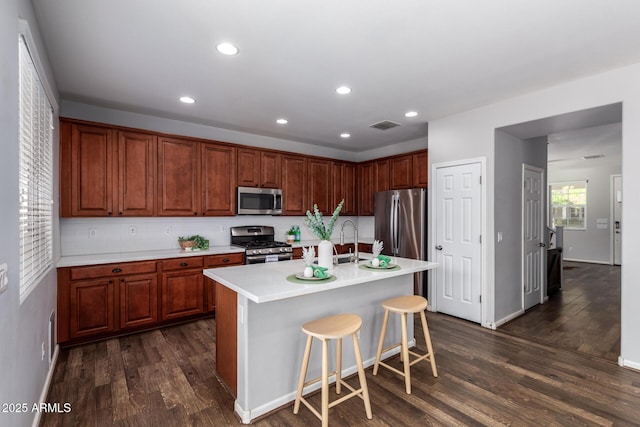 kitchen with sink, a breakfast bar area, appliances with stainless steel finishes, an island with sink, and dark hardwood / wood-style flooring