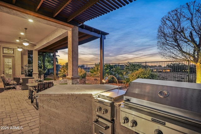 patio terrace at dusk featuring ceiling fan, area for grilling, and grilling area