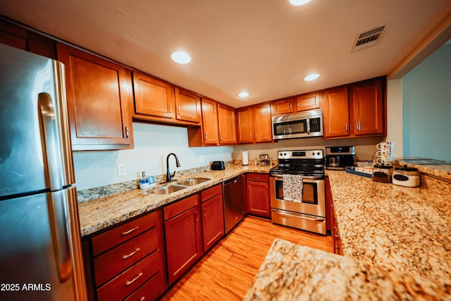 kitchen featuring visible vents, a sink, stainless steel appliances, light wood-style floors, and light stone countertops