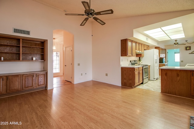 kitchen featuring visible vents, stainless steel range with electric stovetop, arched walkways, brown cabinetry, and ceiling fan