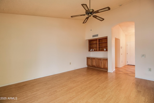 spare room with visible vents, a ceiling fan, arched walkways, light wood-style floors, and a high ceiling