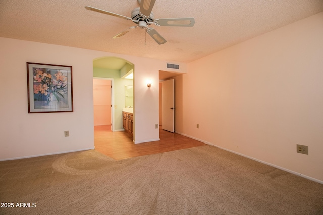 interior space featuring a ceiling fan, visible vents, arched walkways, a textured ceiling, and light carpet