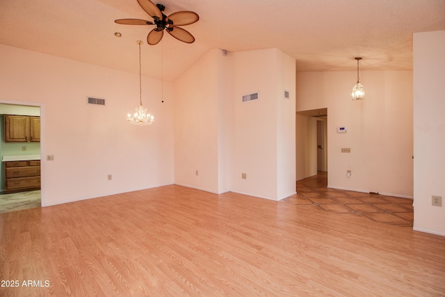 unfurnished living room with high vaulted ceiling, ceiling fan with notable chandelier, visible vents, and light wood-type flooring