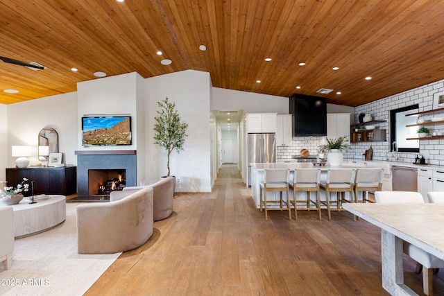 living room featuring a tile fireplace, lofted ceiling, wooden ceiling, and light wood-type flooring