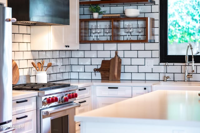 kitchen with sink, white cabinetry, refrigerator, high end stove, and exhaust hood