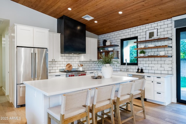 kitchen featuring a kitchen island, high quality fridge, white cabinetry, a kitchen breakfast bar, and exhaust hood