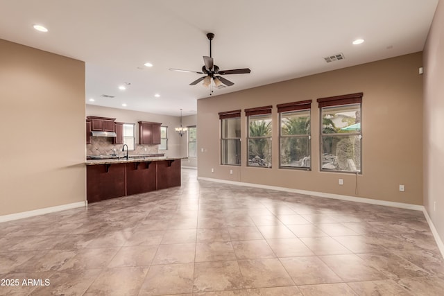 interior space with light stone countertops, sink, a kitchen breakfast bar, pendant lighting, and ceiling fan with notable chandelier