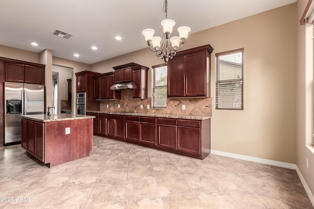 kitchen featuring pendant lighting, an inviting chandelier, decorative backsplash, an island with sink, and appliances with stainless steel finishes