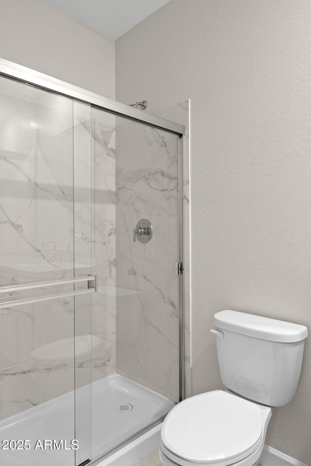 bathroom with a textured wall, a marble finish shower, and toilet