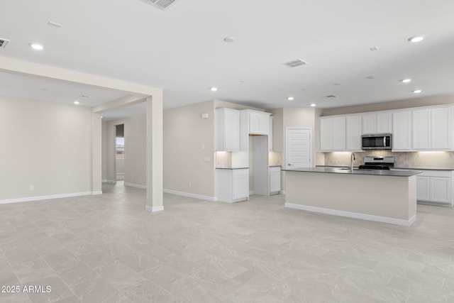 kitchen featuring tasteful backsplash, dark countertops, open floor plan, stainless steel appliances, and a sink