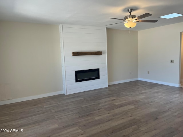 unfurnished living room with ceiling fan, dark wood-type flooring, and a large fireplace