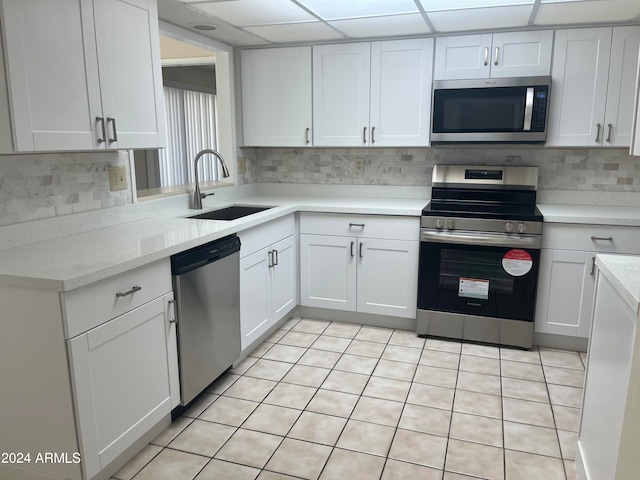 kitchen with tasteful backsplash, sink, white cabinets, a paneled ceiling, and stainless steel appliances