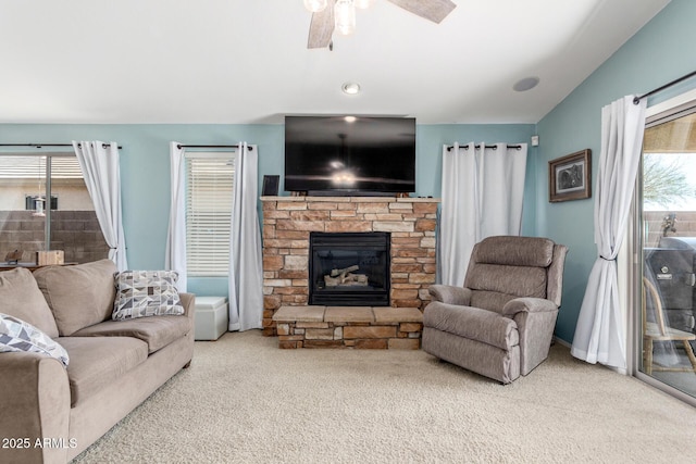 carpeted living room with a stone fireplace, vaulted ceiling, and a ceiling fan