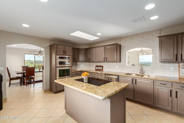 kitchen with light stone countertops, stainless steel appliances, ceiling fan, and a center island