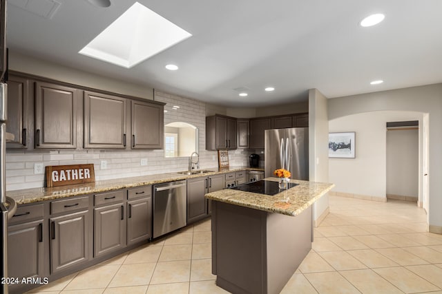 kitchen with appliances with stainless steel finishes, light tile floors, a kitchen island, tasteful backsplash, and light stone countertops