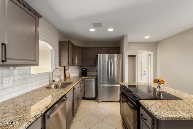 kitchen with tasteful backsplash, appliances with stainless steel finishes, sink, and light stone countertops