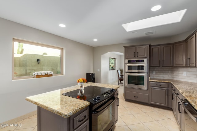 kitchen with a skylight, black electric range oven, light tile floors, stainless steel double oven, and light stone countertops