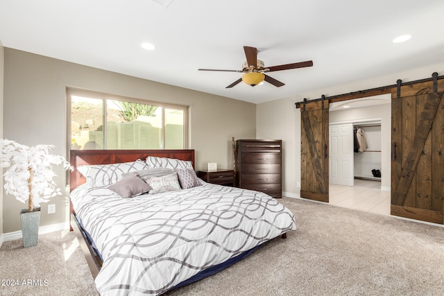 carpeted bedroom with a barn door, ceiling fan, and a closet