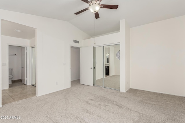 unfurnished bedroom featuring ensuite bath, ceiling fan, light carpet, vaulted ceiling, and a closet