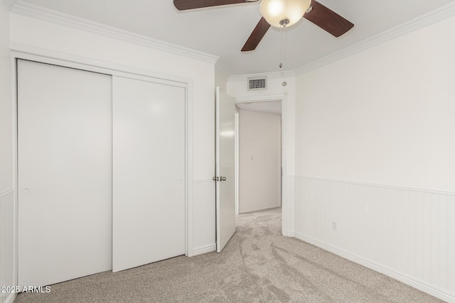 unfurnished bedroom featuring crown molding, light carpet, ceiling fan, and a closet