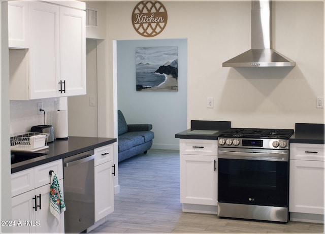 kitchen featuring stainless steel appliances, white cabinetry, sink, light hardwood / wood-style flooring, and wall chimney range hood