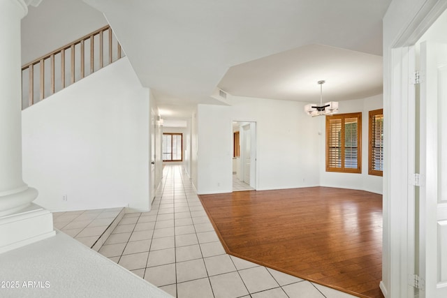 empty room with light tile patterned floors, ornate columns, a wall unit AC, and a notable chandelier