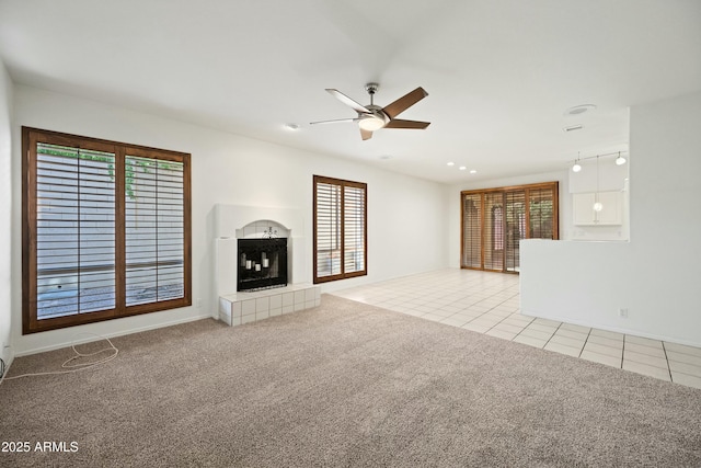 unfurnished living room with light carpet, light tile patterned floors, ceiling fan, and a tiled fireplace