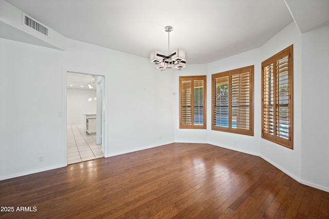 empty room featuring baseboards, wood-type flooring, visible vents, and an inviting chandelier