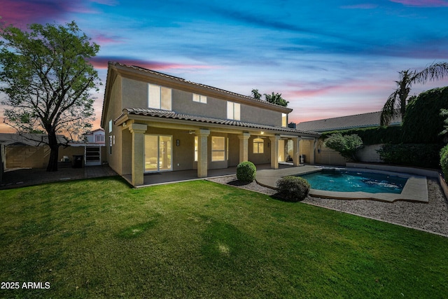 back of property at dusk featuring a lawn, a patio, a fenced backyard, a tiled roof, and stucco siding