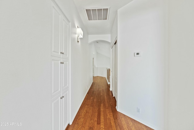 corridor with arched walkways, visible vents, baseboards, and wood finished floors