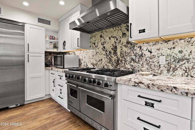 kitchen with white cabinets, wall chimney exhaust hood, backsplash, high quality appliances, and hardwood / wood-style floors