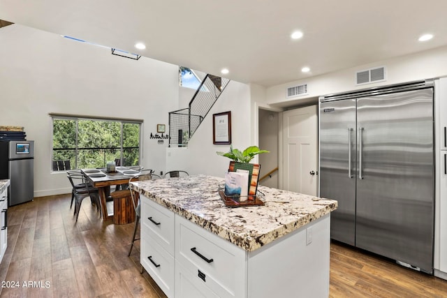 kitchen with a kitchen island, built in refrigerator, white cabinetry, hardwood / wood-style flooring, and light stone countertops