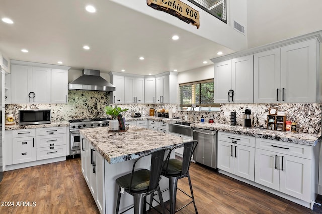 kitchen featuring white cabinets, a kitchen island, dark hardwood / wood-style flooring, stainless steel appliances, and wall chimney range hood