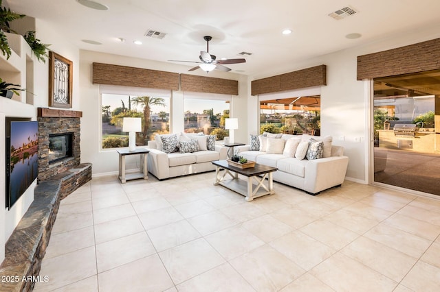 living room featuring a stone fireplace, ceiling fan, and light tile patterned floors