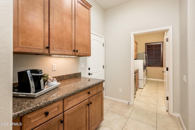 kitchen featuring washing machine and dryer, light tile patterned flooring, and dark stone counters