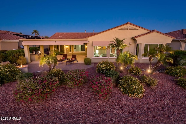 back house at dusk with a patio area and exterior kitchen