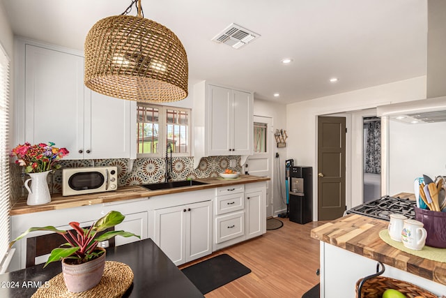 kitchen featuring white cabinetry, light wood-type flooring, pendant lighting, sink, and butcher block countertops