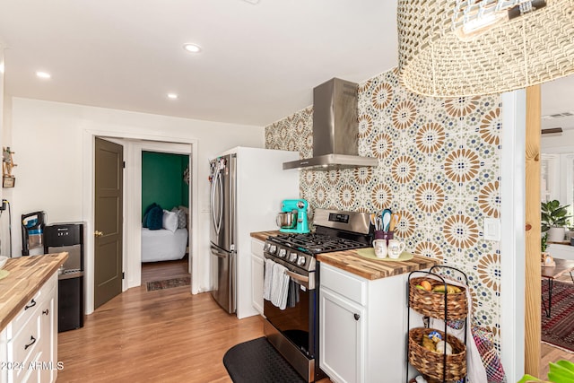 kitchen featuring white cabinetry, wood counters, wall chimney range hood, and stainless steel gas range