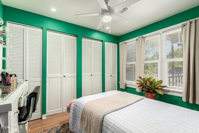 bedroom featuring hardwood / wood-style floors, two closets, and ceiling fan