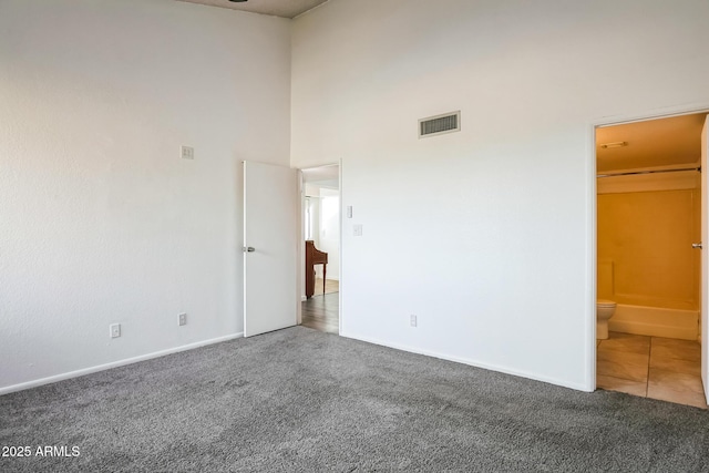 unfurnished bedroom with carpet flooring, a walk in closet, a high ceiling, and ensuite bath